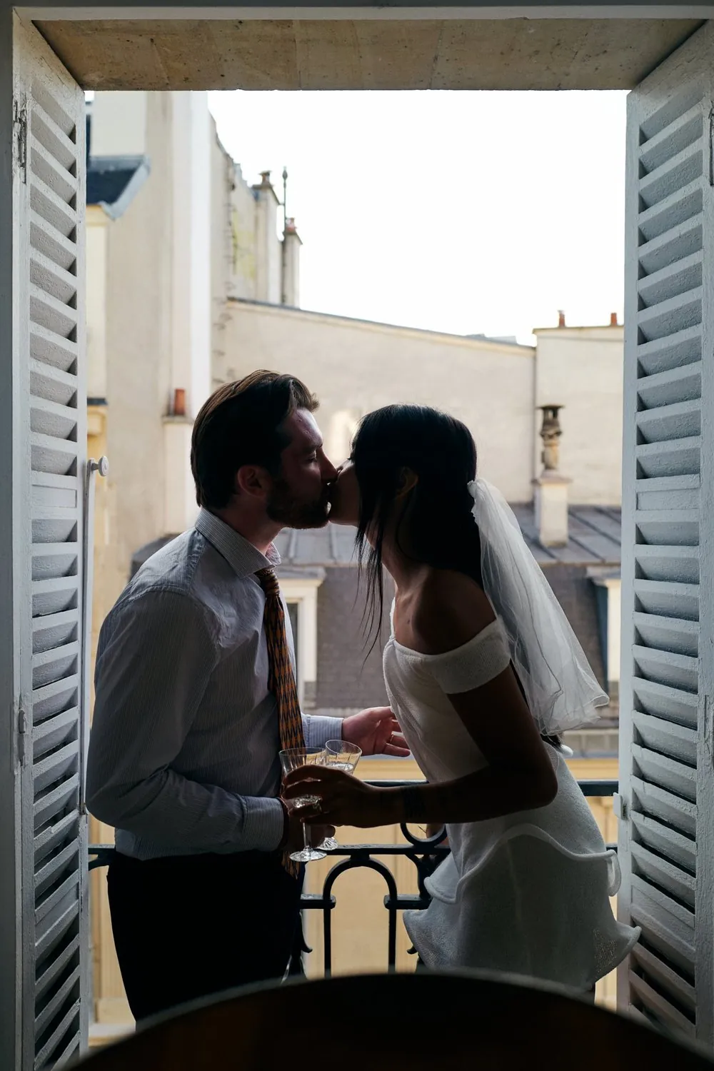 Couple qui s'embrasse sur un balcon parisien, coupes de champagne à la main